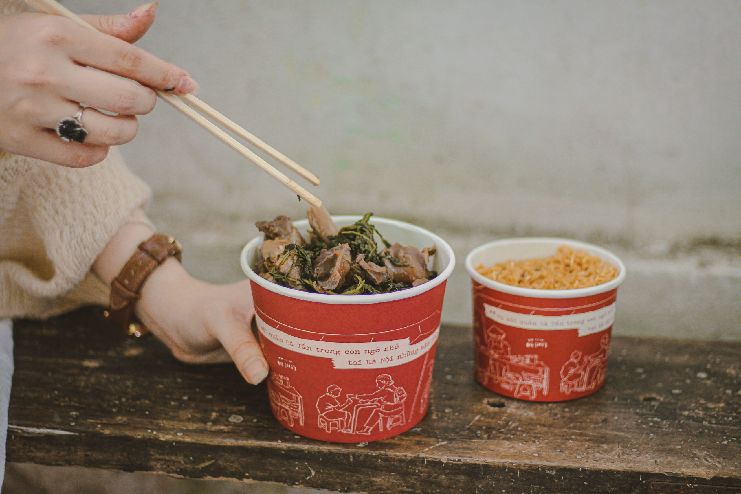 A hand using chopsticks to pick up food from a disposable cup.