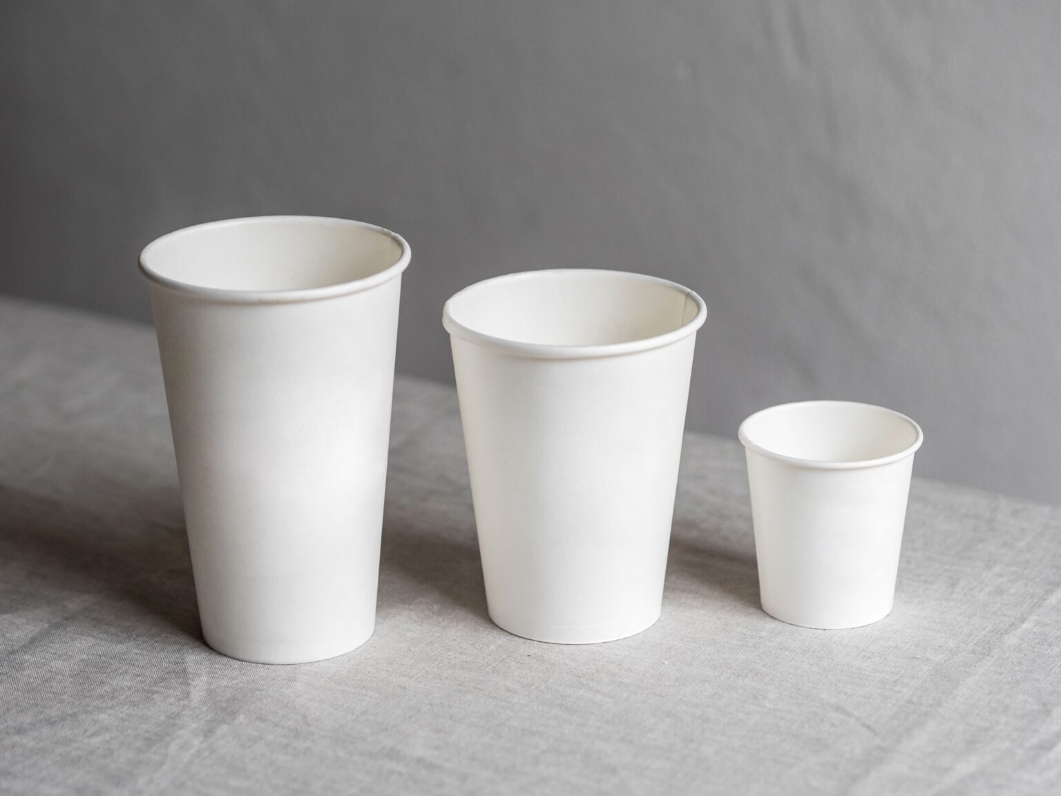 Three white paper cups of different sizes showcasing eco-friendly and recyclable features.